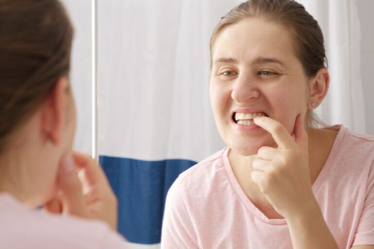 Woman examining her lower teeth in mirror while checking for signs of tooth mobility or damage.