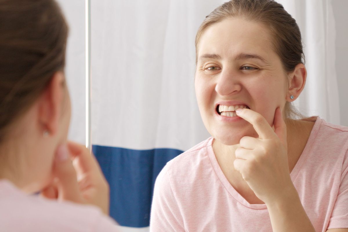 Woman examining her lower teeth in mirror while checking for signs of tooth mobility or damage.