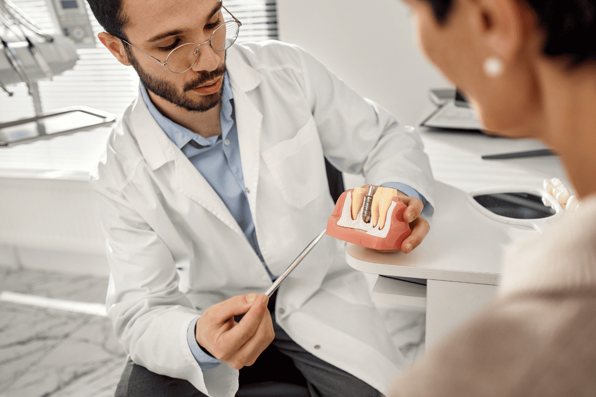 Dentist in San Antonio showing dental implant model to patient during consultation.