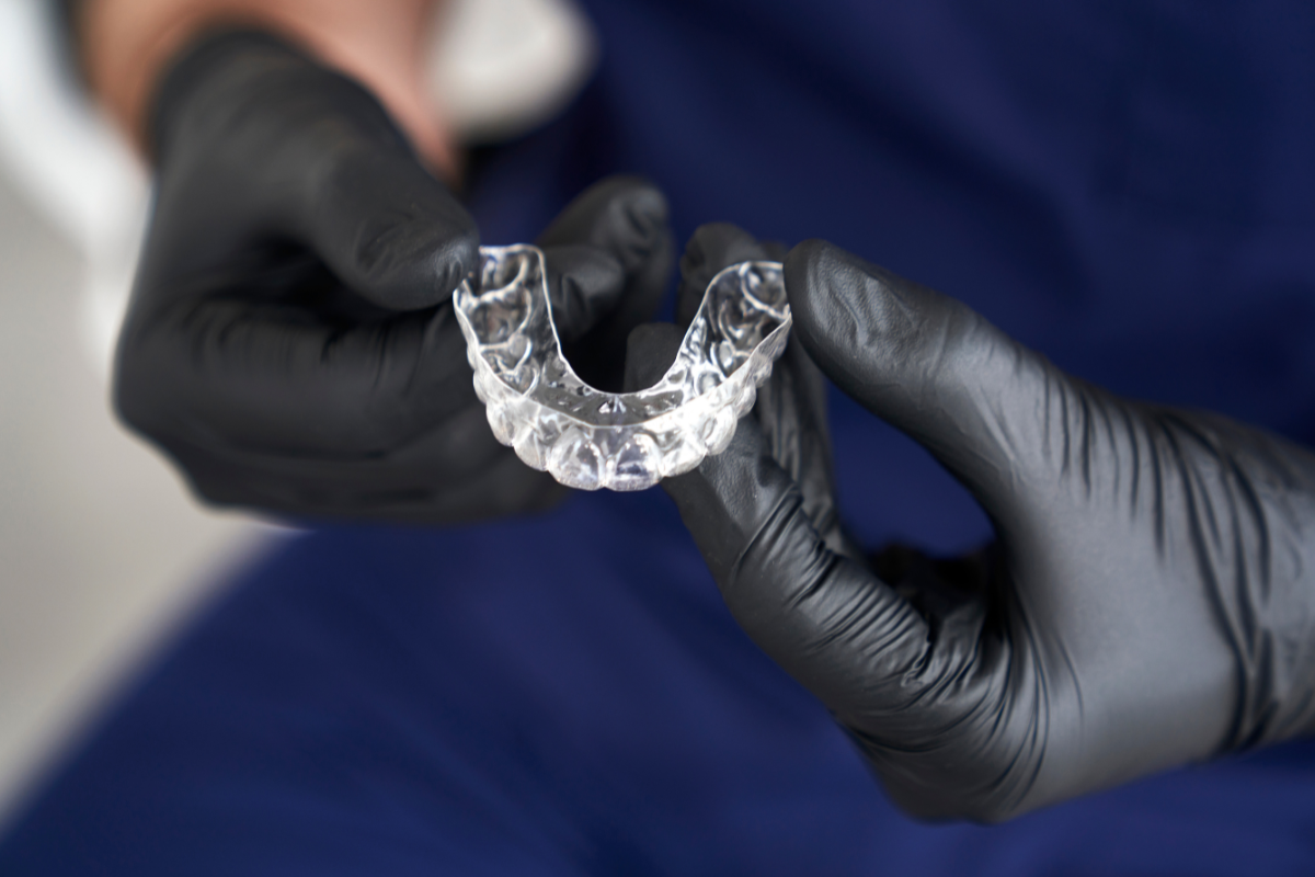 Dentist holding clear Invisalign aligner tray showing dental correction capability.